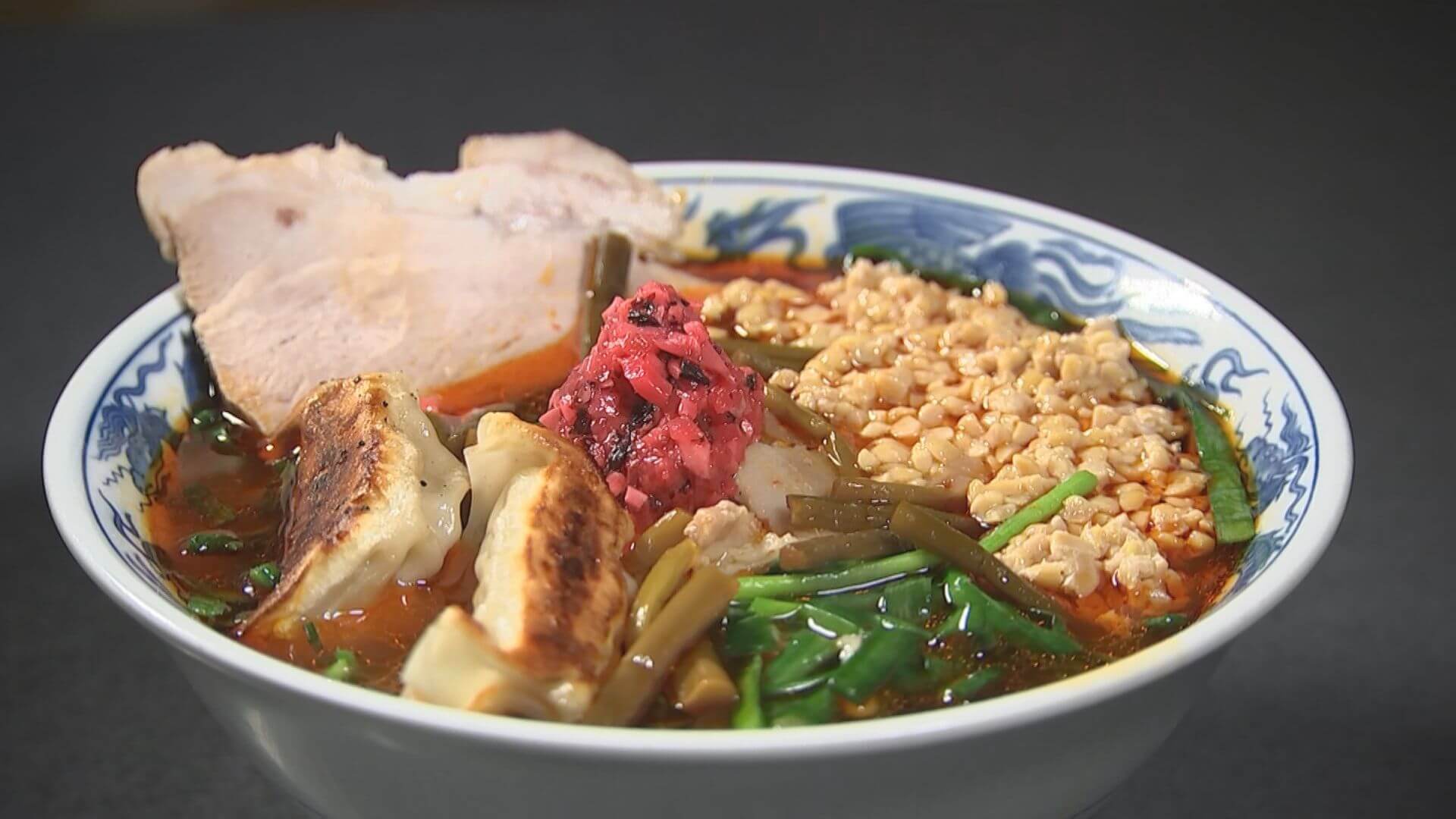 しょう油ベースのたれとたっぷりのラー油に鶏ガラを合わせたスープにちぢれ麺を入れ、餃子、納豆、チャーシューをトッピングした 欲張り満州ニラらーめん　これを見た彦摩呂さん思わず　トッピングの宝石箱や～2023　